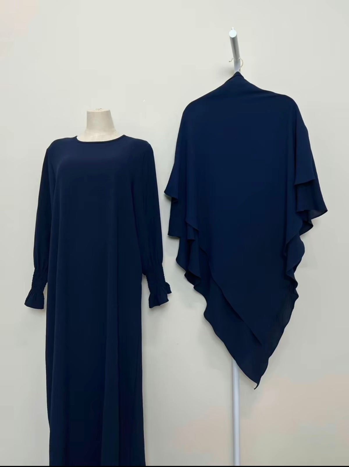 Navy blue dress on a mannequin and draped over a stand against a white background