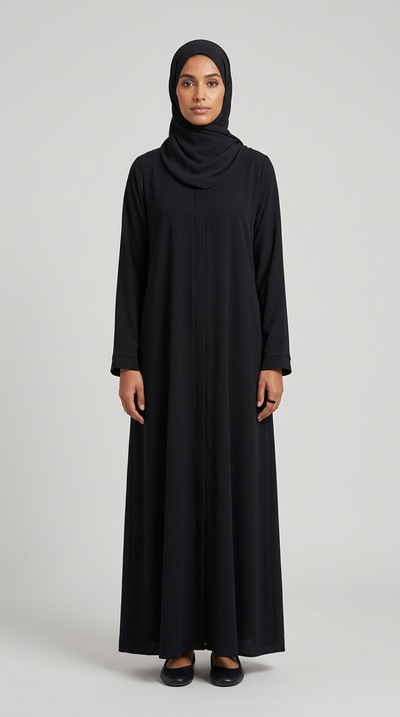 A woman wearing a long-sleeved black abaya and matching black hijab, standing against a solid gray studio background.