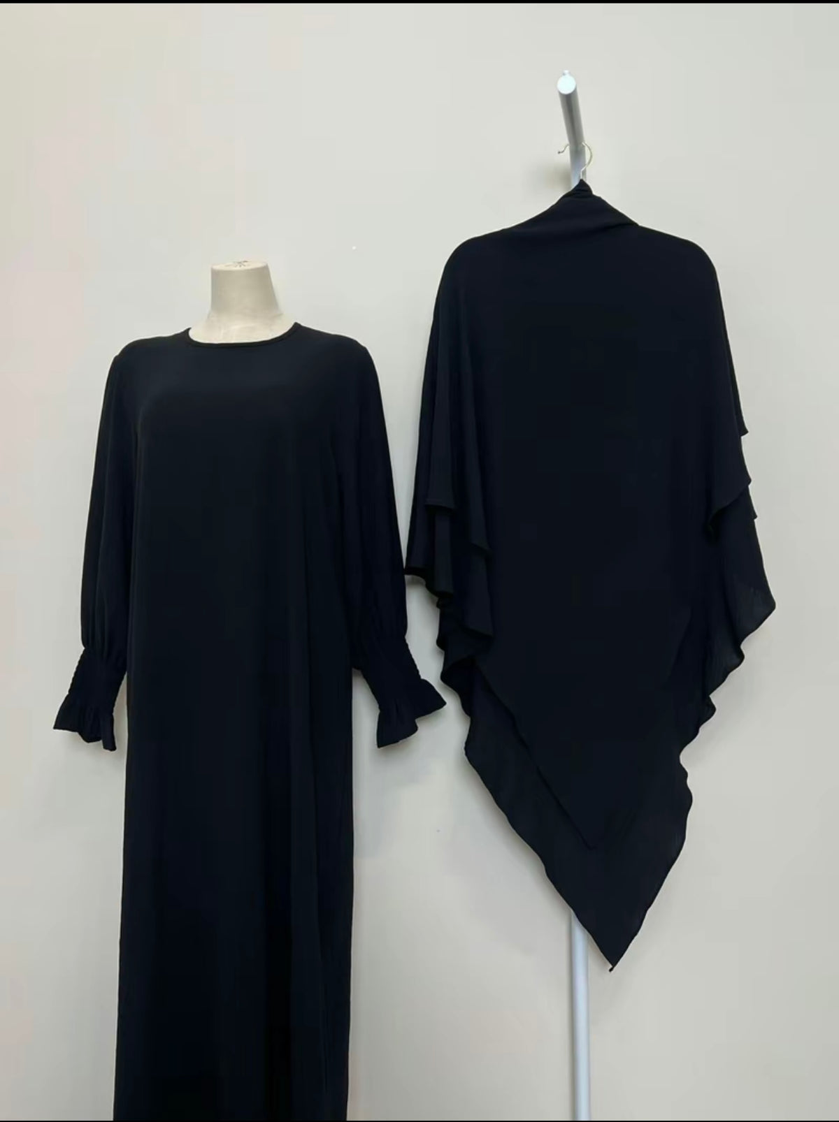 Black dress and black shawl on a mannequin and hanger against a white background