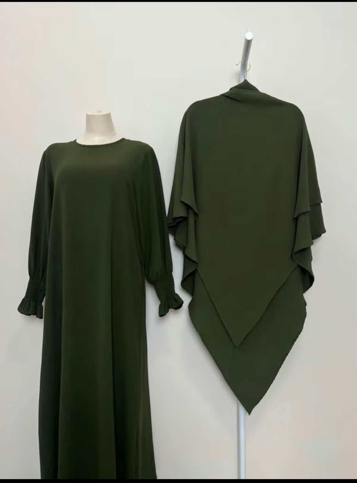 Green dress on a mannequin and draped over a stand against a white background