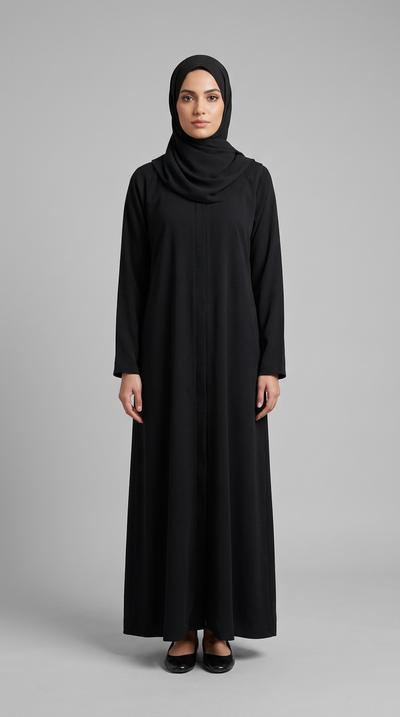 A woman wearing a long-sleeved black abaya and matching black hijab, standing against a solid gray studio background.