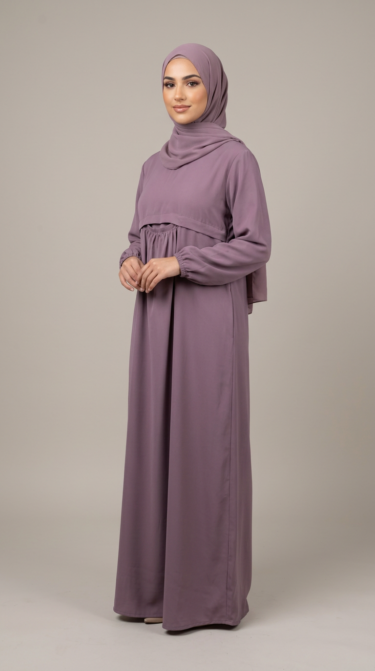 A woman modeling a long-sleeved, floor-length modest dress in dusty purple with a matching hijab, standing against a neutral light gray studio background.
