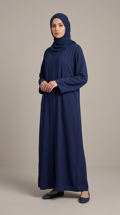 A woman modeling a long-sleeved navy blue modest dress with a matching hijab, standing against a neutral beige studio background.