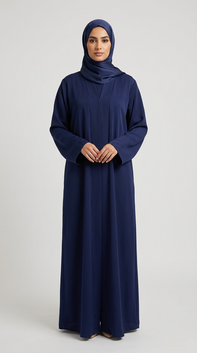 A woman wearing a long-sleeved navy blue abaya and matching hijab, standing against a light gray studio background.