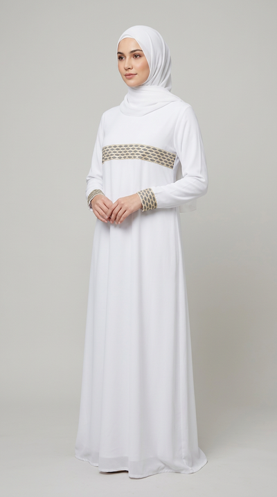 A woman wearing a white long-sleeved hijab dress with a decorative beige and gold woven band at the waist and matching wrist bands, standing against a plain light gray studio background.