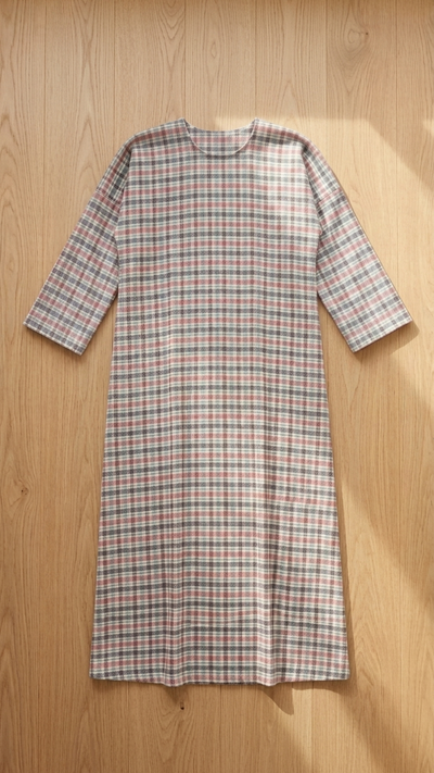 A long-sleeve plaid dress with a crew neck, featuring a pattern of red, green, and white lines on a light beige base, laid flat on a light wood background.