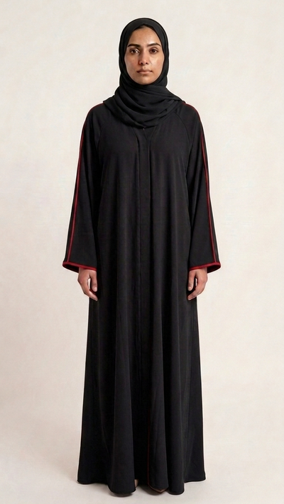 A woman wearing a long black abaya with contrasting red trim on the sleeves and a matching black hijab, standing against a plain light beige studio background.