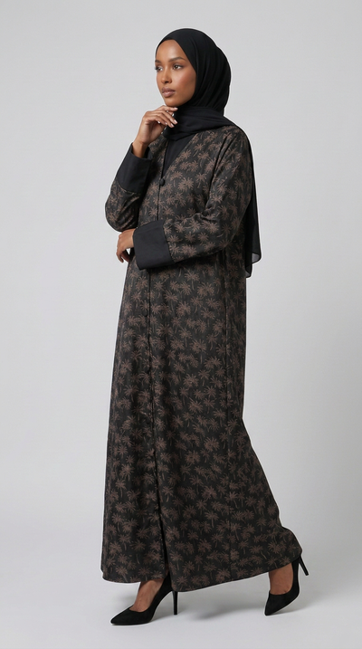A woman modeling a long-sleeved black and brown floral-patterned abaya with a matching black hijab, standing against a light gray studio background.