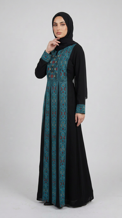 A woman wearing a long black modest dress with teal and red embroidered vertical panels and a matching black hijab, standing against a light gray studio background.