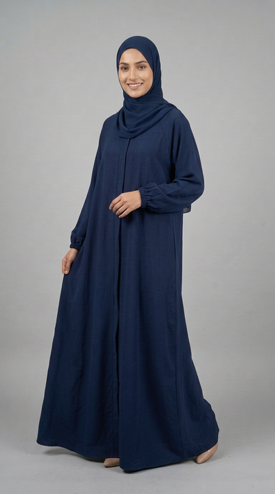 A woman wearing a long navy blue abaya and matching hijab, standing against a neutral gray studio background.