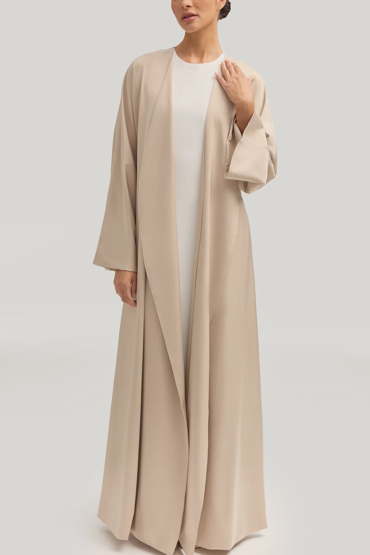 Woman wearing a long beige cardigan over a white top on a light gray background