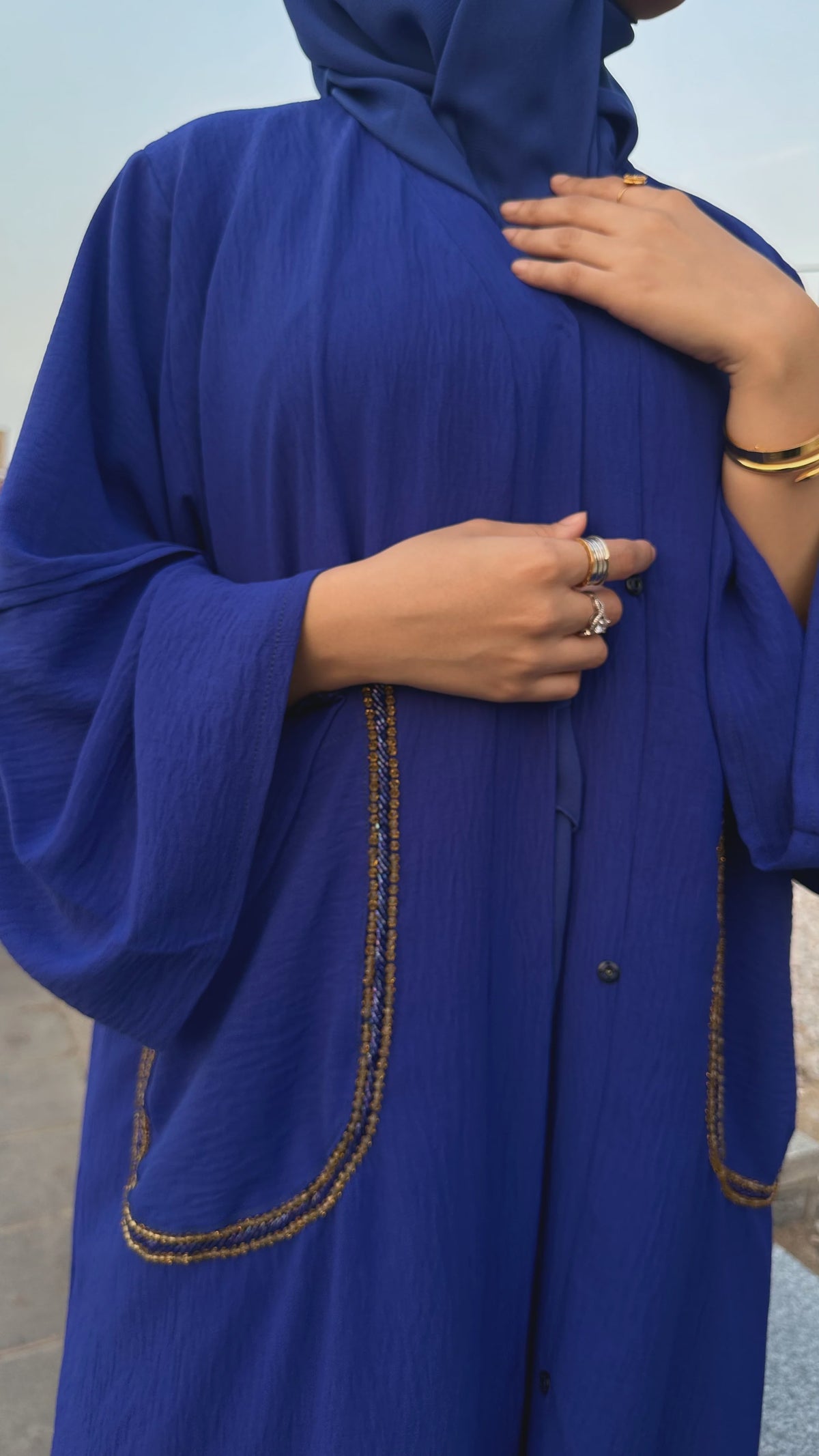 Person wearing a blue abaya with gold embroidery, standing against a neutral background.