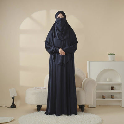 Woman in a long dark blue dress standing in a room with beige walls and white furniture.
