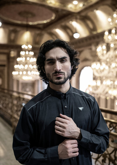 Man wearing a black shirt with a logo in an elegant interior setting with chandeliers.
