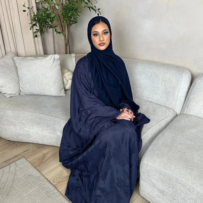 Woman in a navy abaya sitting on a gray sofa in a living room.
