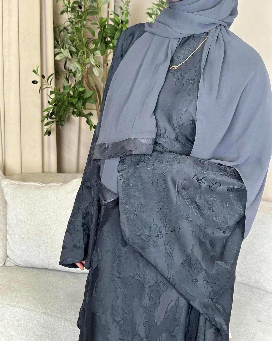 Person wearing a gray hijab and dress with a neutral background