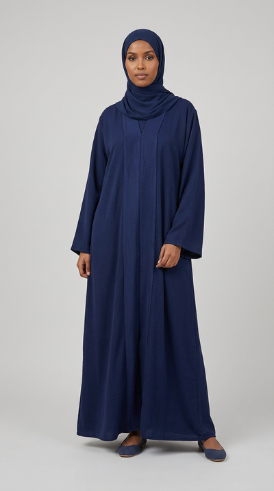 A woman wearing a long navy blue abaya and matching hijab, standing against a light gray studio background.