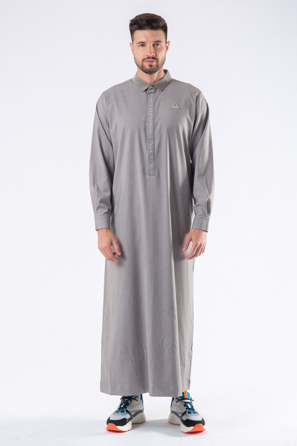 A man standing and modeling a gray traditional thobe with a V-neck and long sleeves.